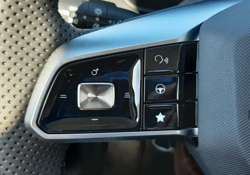 Gros plan sur les commandes gauche du volant perforé du MG ZS 1.5 Hybrid+ 197ch, finition noire brillante et argentée.