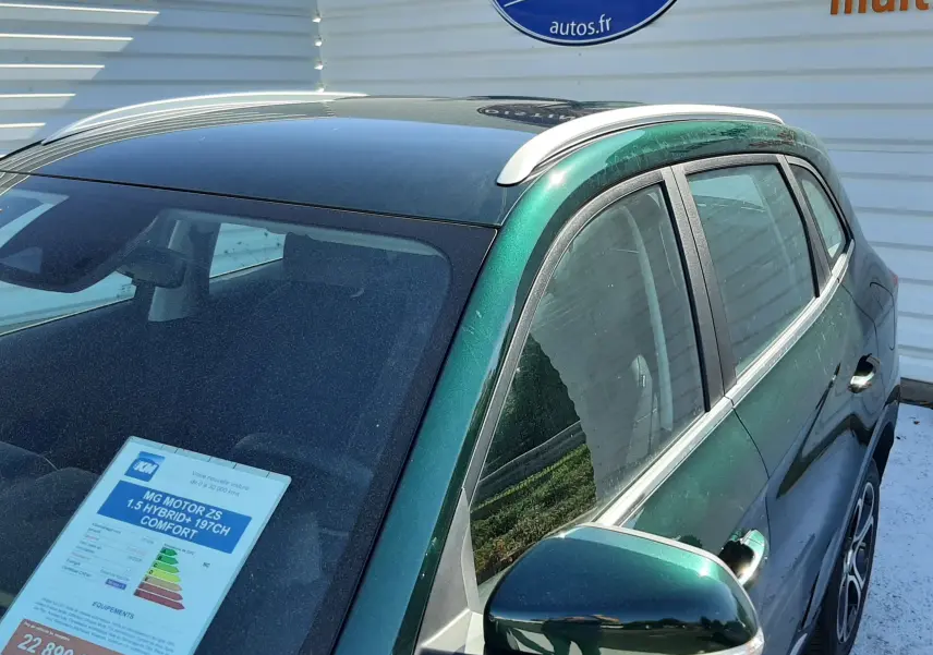 Vue 3/4 avant droit du MG MOTOR ZS 1.5 HYBRID+ vert émeraude avec toit noir et barres de toit argentées.