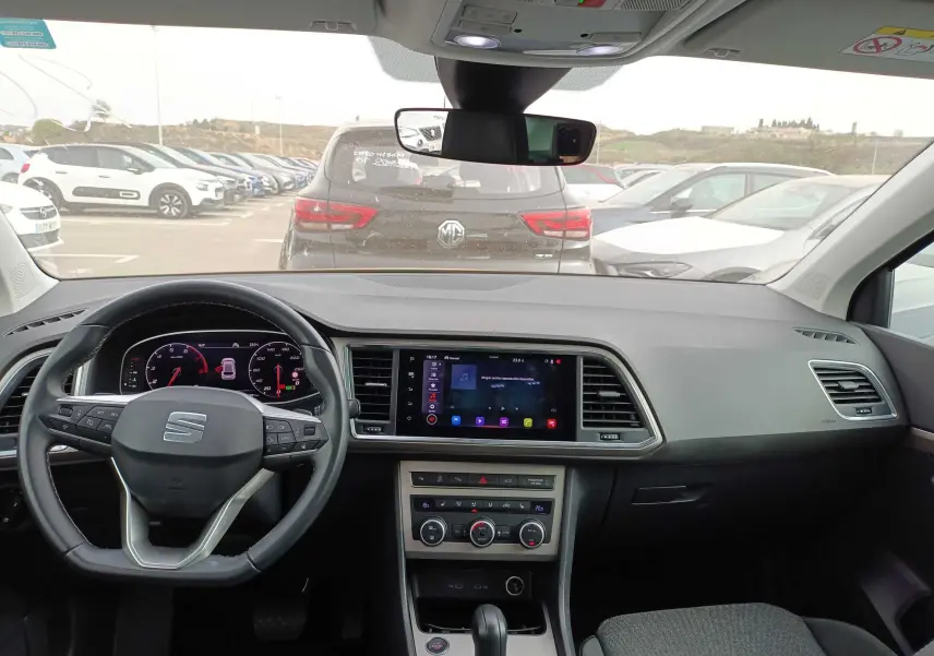 Vue intérieure avant du tableau de bord et volant du SEAT Ateca gris foncé, avec écran tactile central et commandes climatisation visibles.