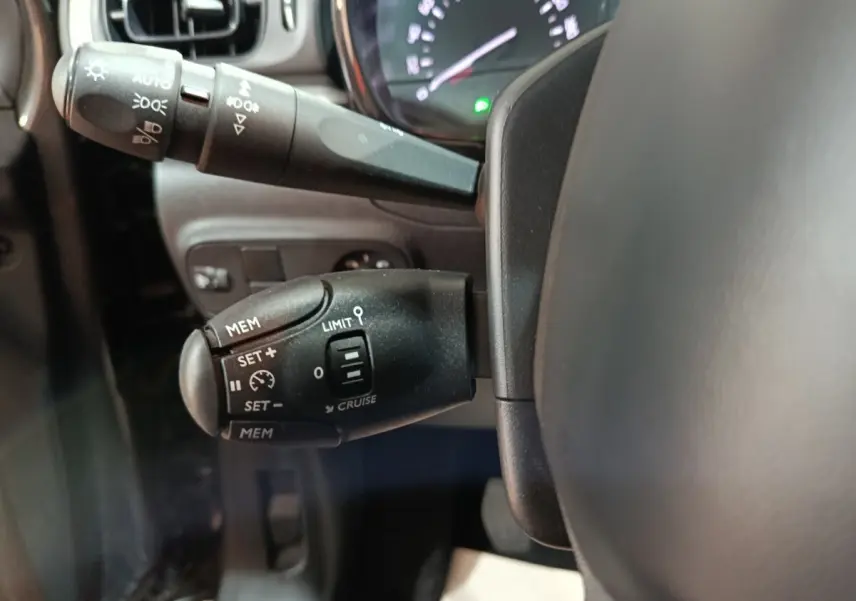 Gros plan sur la commande de régulateur de vitesse à gauche du volant dans l'habitacle d'une Citroën C3 gris foncé 2024.