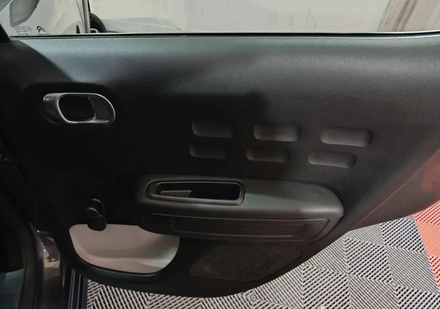 Vue intérieure de la porte avant gauche gris foncé de la Citroën C3 2024 avec poignée intégrée et haut-parleur visible.