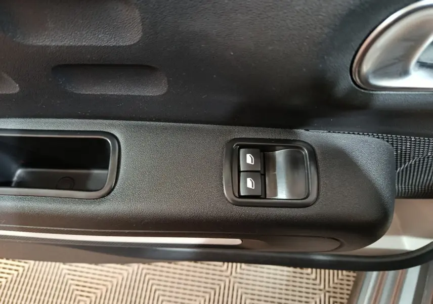 Gros plan sur les commandes des vitres électriques côté conducteur d'une Citroën C3 gris foncé, intérieur noir.