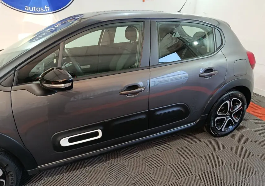 Vue de profil côté gauche d'une Citroën C3 2024 gris foncé avec protections latérales noires et jantes bicolores.