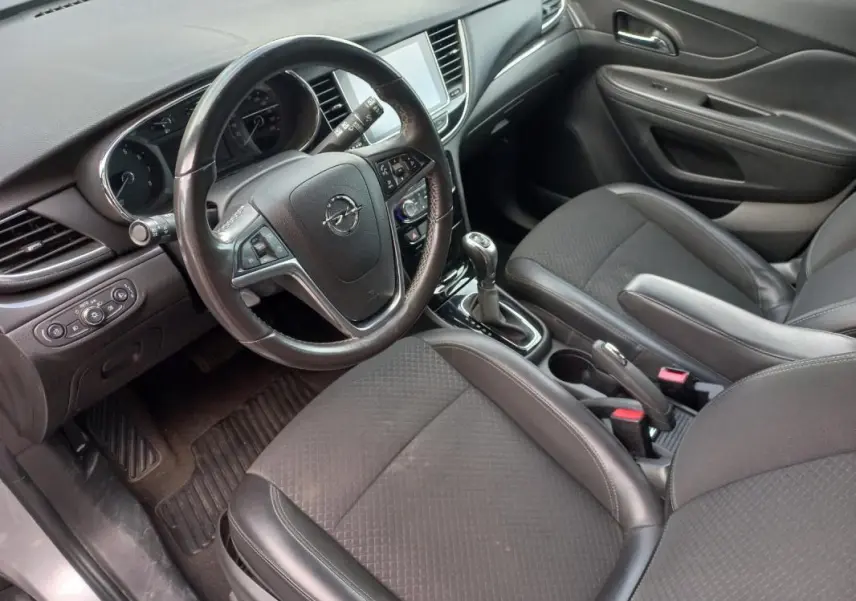 Vue intérieure côté conducteur de l’Opel Mokka X 2017, montrant le volant, la console centrale et les sièges en tissu gris foncé.