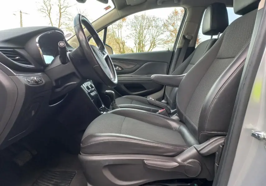 Vue intérieure côté conducteur de l’Opel Mokka X 2017, sièges tissu et cuir noirs avec accoudoir central.