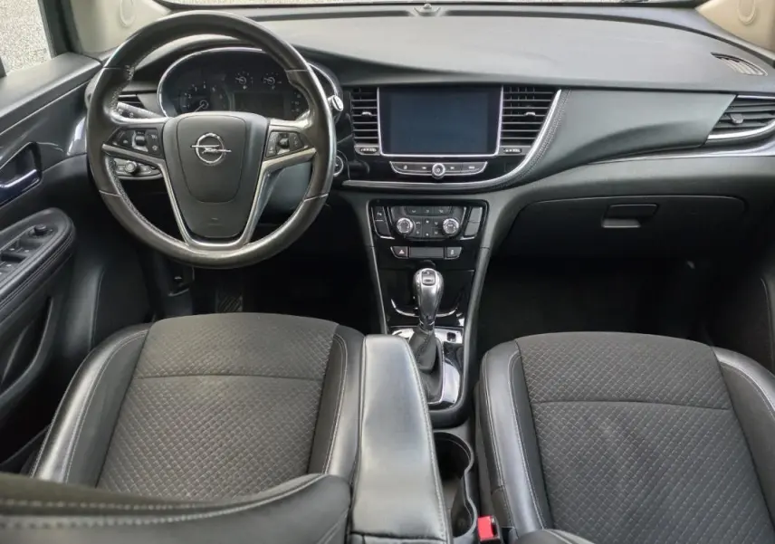 Vue intérieure avant de l'Opel Mokka X 2017, montrant le volant, tableau de bord et sièges noirs en tissu et cuir.