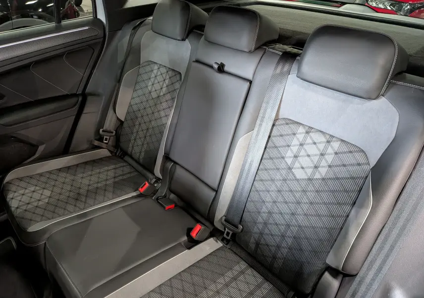 Vue intérieure arrière du Volkswagen Tiguan 2024, sièges en cuir gris et tissu à motif géométrique, ceintures de sécurité visibles.