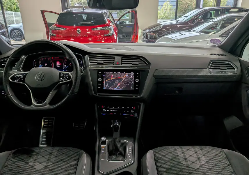 Vue intérieure avant du Volkswagen Tiguan 2024 en reflet d'argent, avec tableau de bord numérique et écran tactile central allumé.