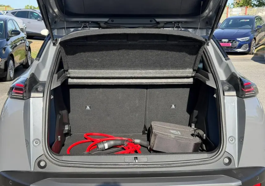 Coffre ouvert d’un Peugeot e-2008 gris Artense, vue arrière, avec câble de recharge électrique rouge visible.