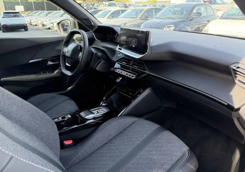 Intérieur avant droit du Peugeot e-2008 2025, montrant sièges tissu gris et tableau de bord avec écran tactile central.