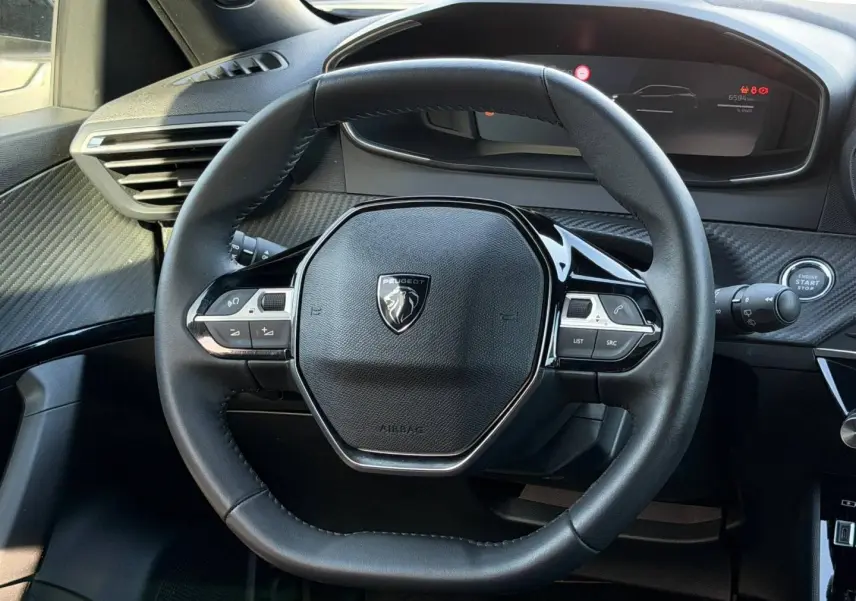 Vue rapprochée du volant multifonction noir de la Peugeot e-2008 2025 avec tableau de bord numérique en arrière-plan.