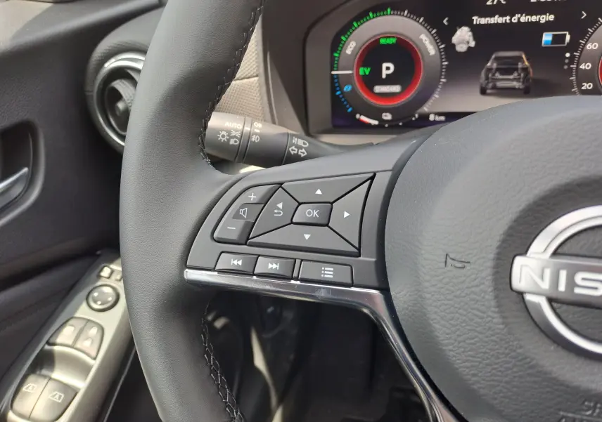 Gros plan sur le volant noir et les commandes intégrées du tableau de bord numérique d'un Nissan Juke Hybrid gris squale 2025.