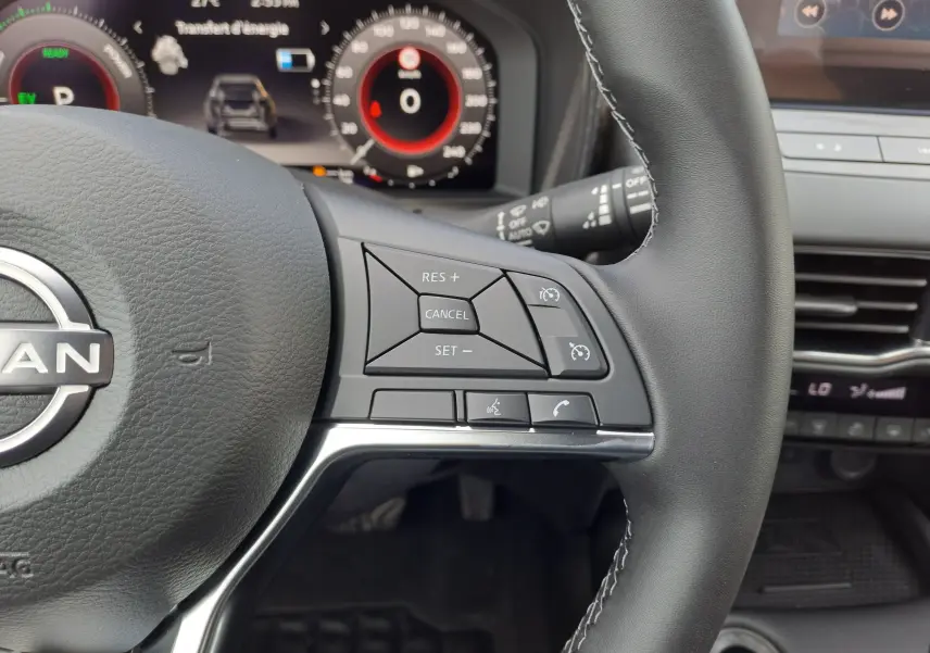 Gros plan sur le volant noir du Nissan Juke Hybrid 2025, avec commandes de régulateur et tableau de bord numérique en arrière-plan.