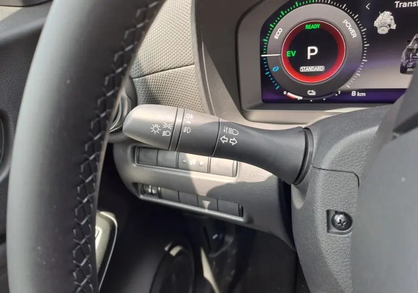 Gros plan sur la manette des clignotants à gauche du volant du Nissan Juke Hybrid gris, avec tableau de bord numérique visible.