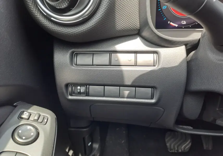 Détail intérieur côté gauche du tableau de bord du Nissan Juke Hybrid 2025 en gris squale, avec commandes et aérateur rond.