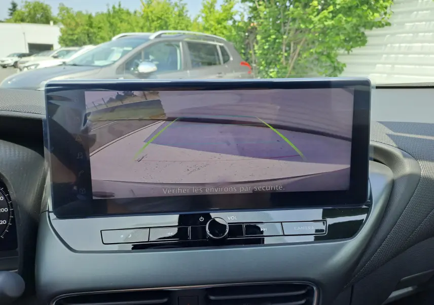 Écran central du Nissan Juke Hybrid 2025 montrant la caméra de recul avec vue sur un parking extérieur.