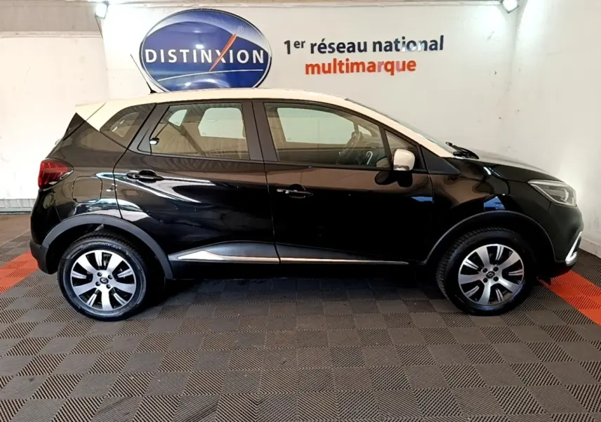 Profil droit d'un Renault Captur Business noir avec toit blanc, jantes alliage et feux arrière visibles en intérieur showroom.