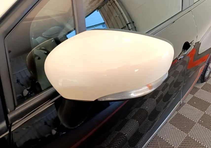 Rétroviseur droit blanc sur Renault Captur noir, vue rapprochée du côté avant droit avec poignée de porte visible.
