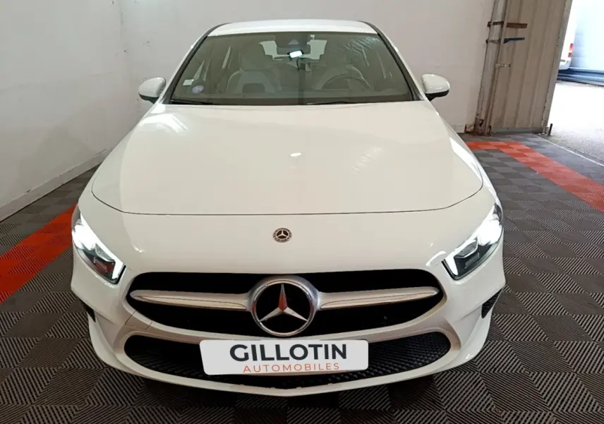 Vue avant d'une Mercedes Classe A Berline blanche avec phares LED allumés dans un garage.