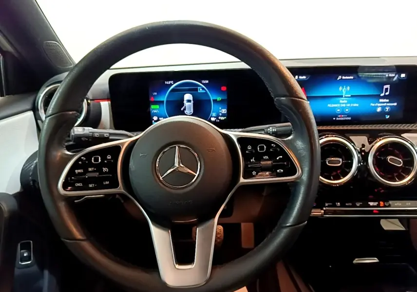 Vue intérieure centrée sur le volant cuir multifonctions et le tableau de bord numérique de la Mercedes Classe A blanche.