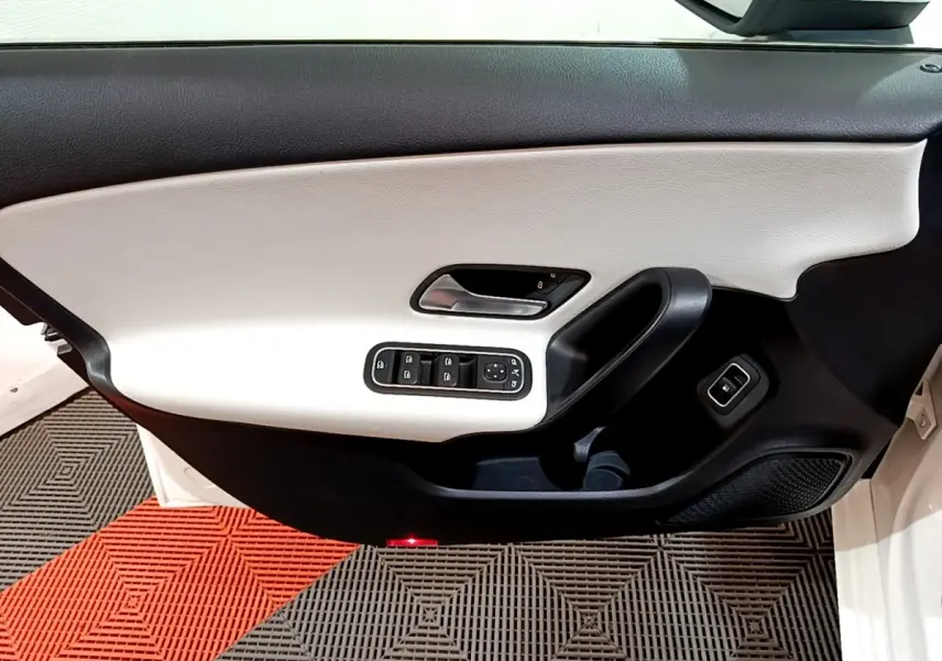 Gros plan sur la porte avant gauche blanche d'une Mercedes Classe A 250 e Business Line, avec commandes électriques et garniture bicolore.