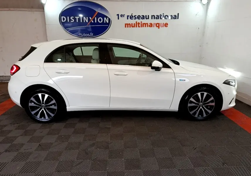 Vue latérale droite d'une Mercedes Classe A Berline blanche, hybride rechargeable, avec jantes alliage et feux arrière allumés.