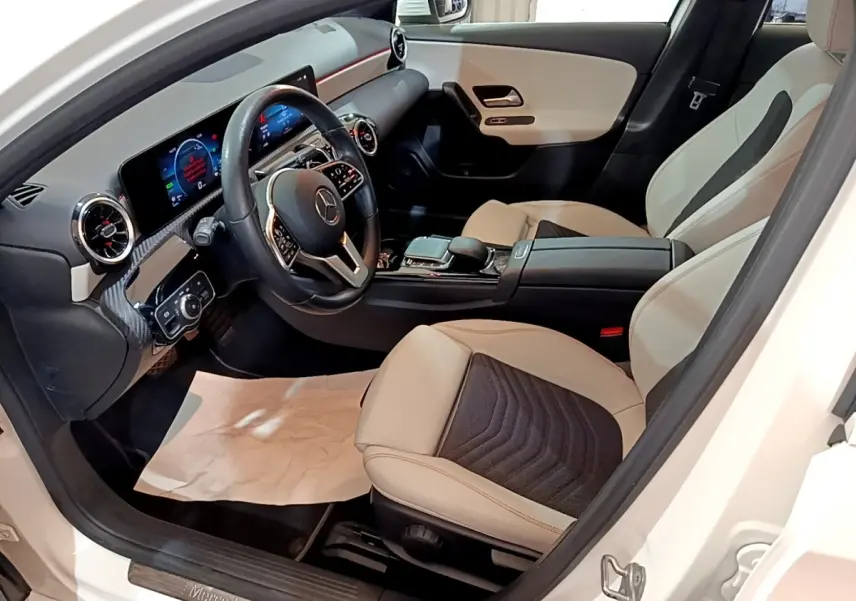 Vue intérieure côté conducteur de la Mercedes Classe A blanche, volant cuir multifonctions et sièges bicolores beige et noir.