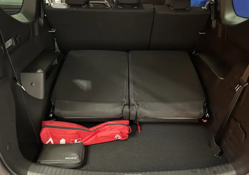 Vue intérieure du coffre du Dacia Jogger gris schiste avec sièges arrière rabattus et trousse de secours rouge visible.