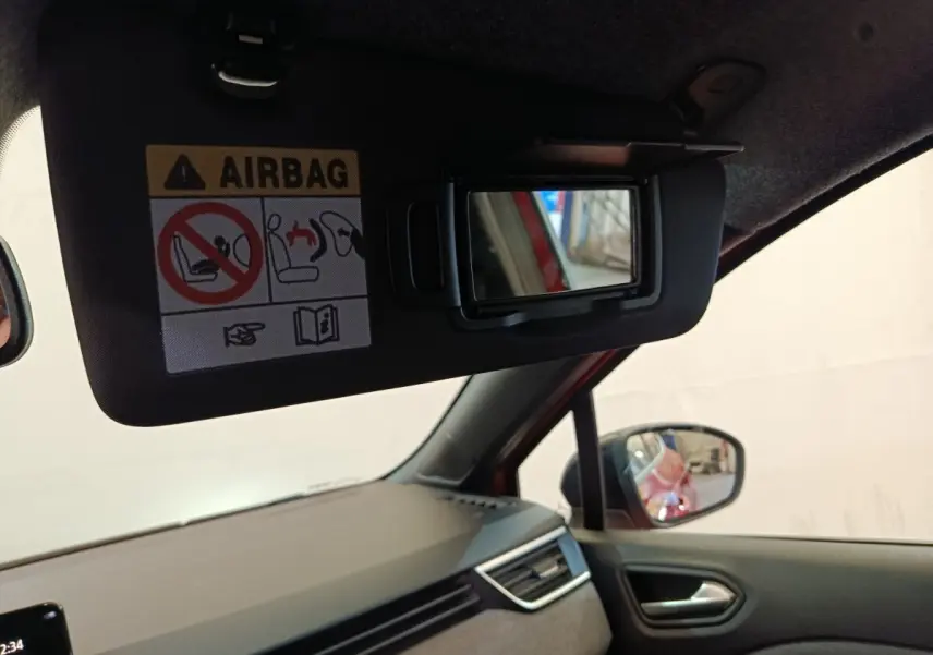 Vue intérieure côté conducteur de la Renault Clio rouge 2024, miroir de pare-soleil ouvert avec avertissement airbag visible.