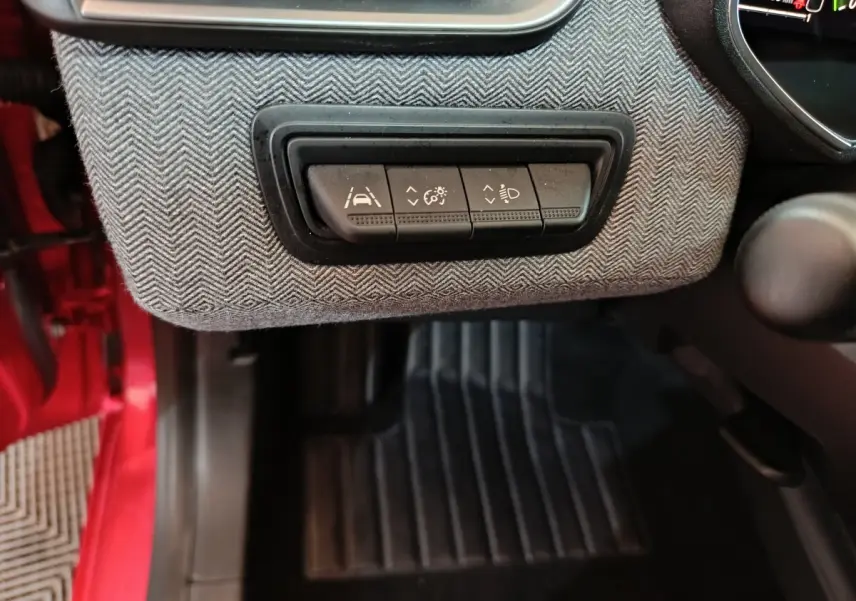 Gros plan sur les commandes d’assistance à la conduite sous le tableau de bord d’une Renault Clio rouge, côté conducteur.