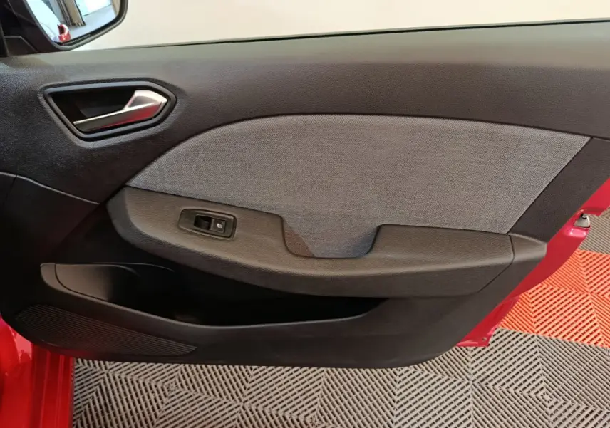 Vue intérieure du panneau de porte avant gauche de la Renault Clio rouge 2024, avec poignée argentée et bouton de commande de vitre.