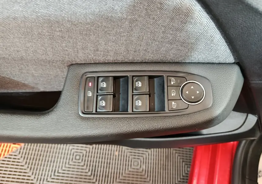 Vue rapprochée des commandes des vitres et rétroviseurs sur la porte côté conducteur d’une Renault Clio rouge 2024.