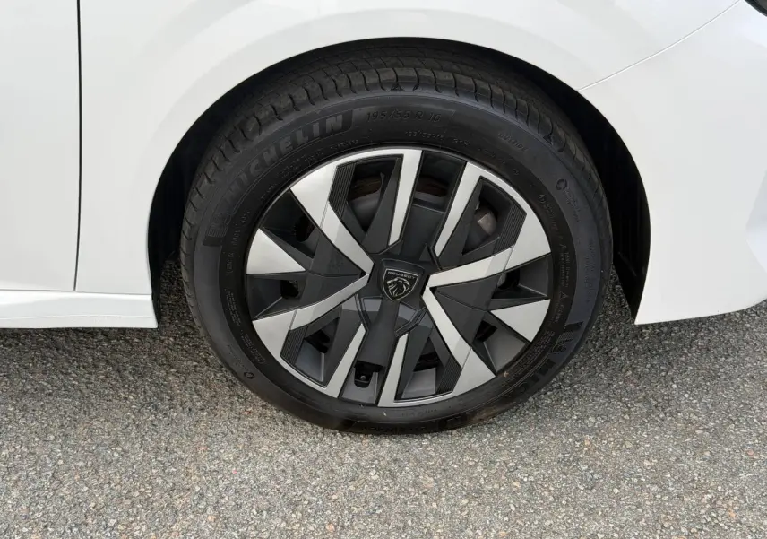 Gros plan sur la roue arrière droite blanche Okénite d'une Peugeot 208 1.2 Hybrid avec jante au design noir et argent.