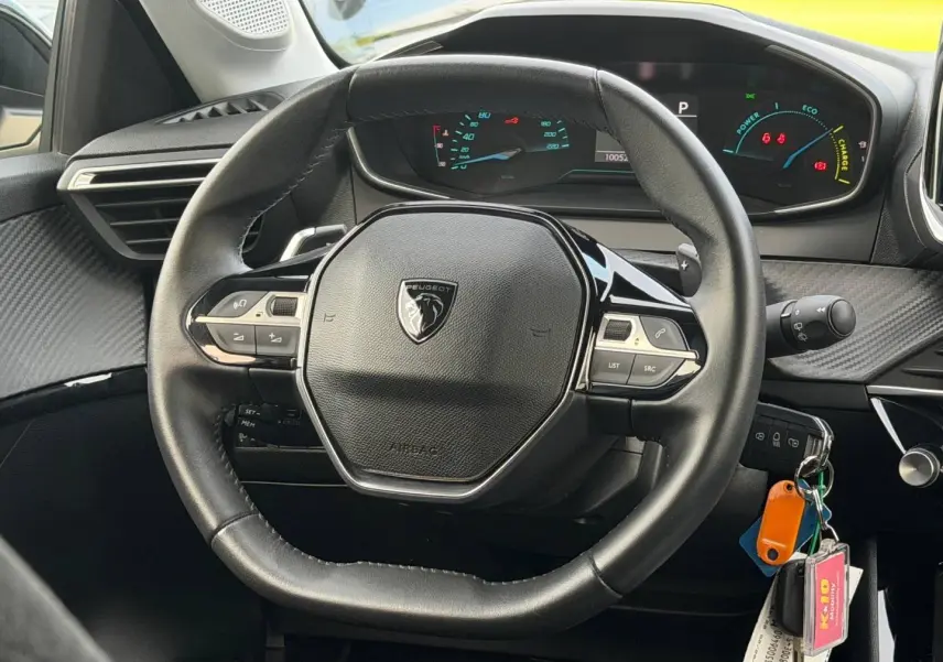 Vue rapprochée du volant noir de la Peugeot 208 1.2 Hybrid 110ch Style avec tableau de bord numérique et clés accrochées.