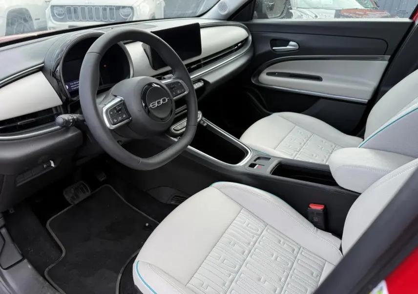 Intérieur avant droit de la FIAT 600 La Prima 2024 rouge, sièges ivoire soft touch avec logo 600 et tableau de bord ivoire.
