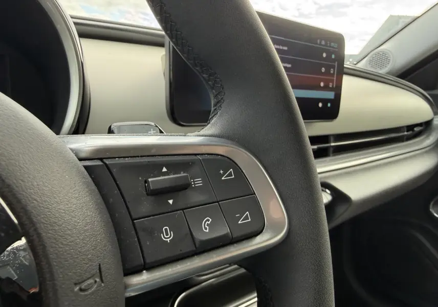 Gros plan sur le volant noir avec commandes intégrées et tableau de bord ivoire de la FIAT 600 rouge 2024 La Prima.