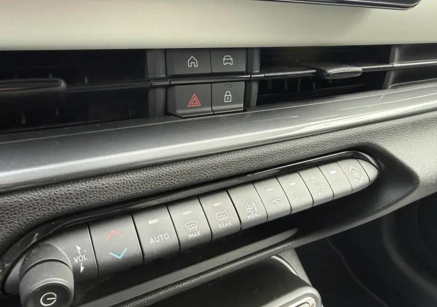 Vue rapprochée de la console centrale noire avec commandes de climatisation et boutons multifonctions sur Fiat 600 rouge 2024