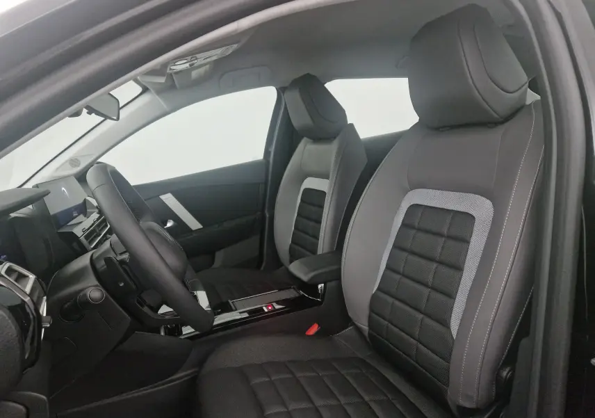 Vue intérieure côté conducteur de la Citroën C4 2025 noire, sièges tissu noir et gris avec console centrale moderne.