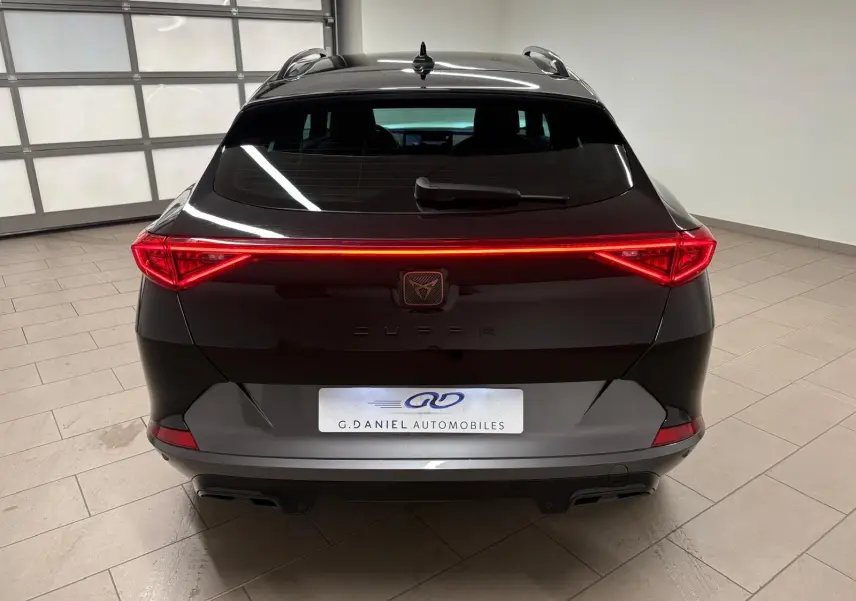 Vue arrière d'un CUPRA Formentor noir minuit 2024 avec feux arrière LED continus et hayon électrique en intérieur showroom.