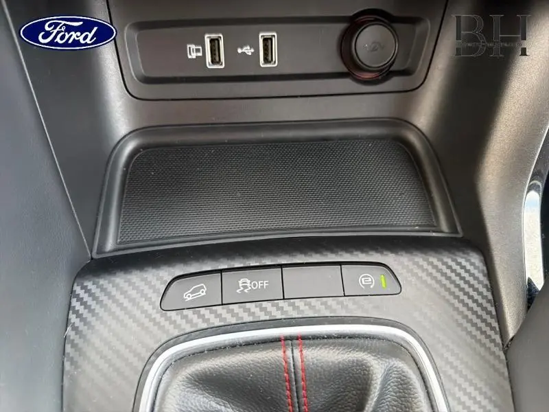 Gros plan sur la console centrale avec prises USB, bouton de contrôle de traction et frein de stationnement, finition carbone.