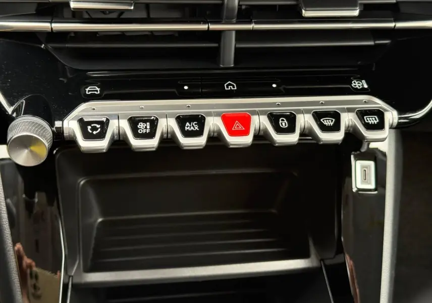 Vue rapprochée des commandes centrales avec boutons argentés et rouge sur tableau de bord noir brillant d'une Peugeot 208.