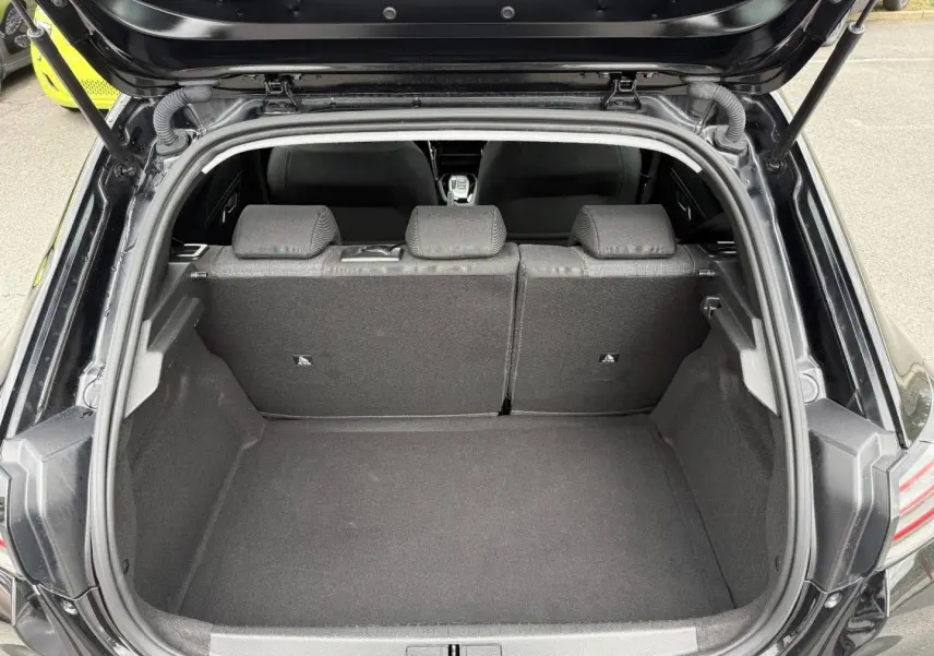 Coffre ouvert vu de l'arrière d'une Peugeot 208 noire Perla Nera avec banquette arrière en tissu gris.