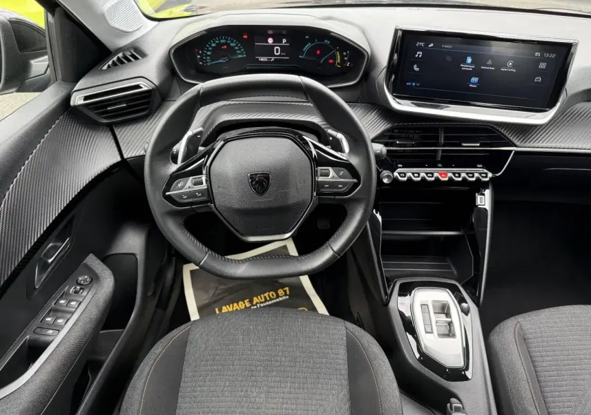 Vue intérieure avant centrée sur le volant noir et le tableau de bord numérique de la Peugeot 208 1.2 Hybrid 2025.