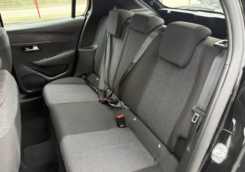 Vue intérieure de la banquette arrière noire et grise avec surpiqûres orange dans une Peugeot 208 2025, porte ouverte côté droit.