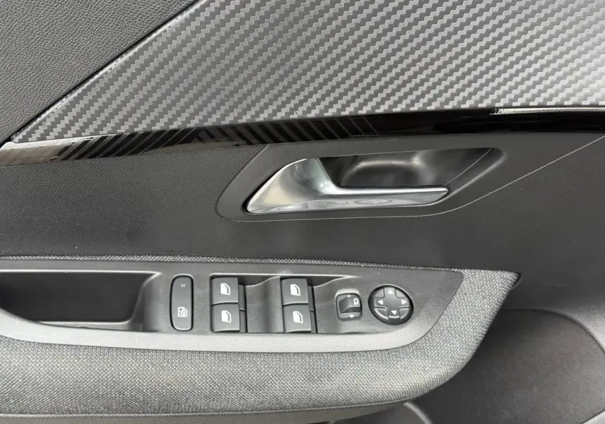 Gros plan sur la porte côté gauche intérieure de la Peugeot 208 1.2 Hybrid noire avec commandes des vitres et poignée argentée.