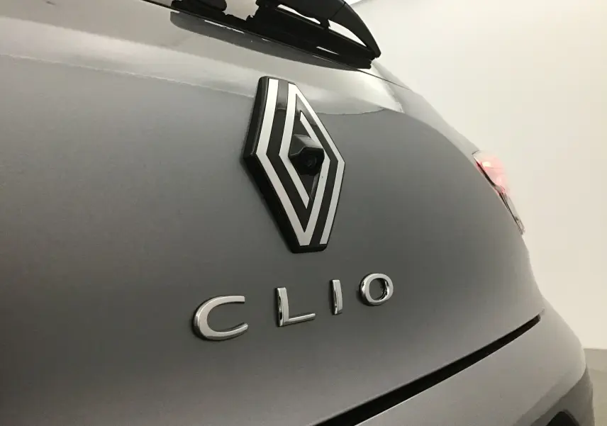 Gros plan sur l'arrière gris schiste d'une Renault Clio V mettant en valeur le logo et la caméra de recul intégrée.