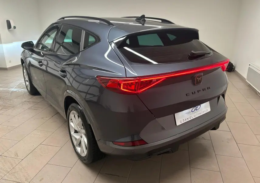 Vue 3/4 arrière droite du CUPRA Formentor gris magnétique 2024 avec feux arrière allumés et hayon fermé en intérieur.