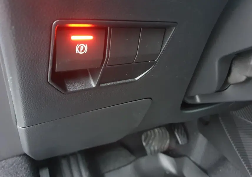 Gros plan sur le bouton de frein à main électronique allumé dans l'habitacle noir du Dacia Duster blanc glacier 2025.