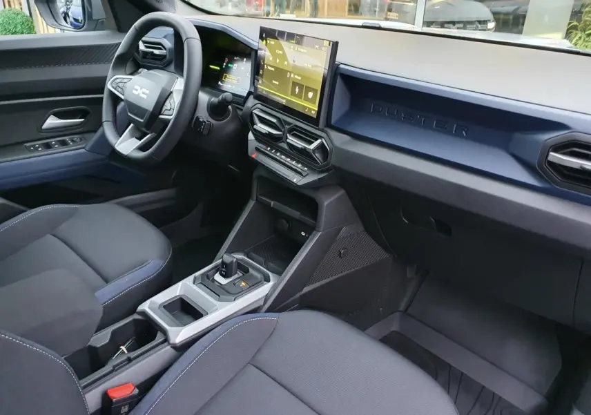 Vue intérieure côté conducteur du tableau de bord du Dacia Duster 1.6 Hybrid 140 blanc glacier avec écran tactile et volant multifonction.