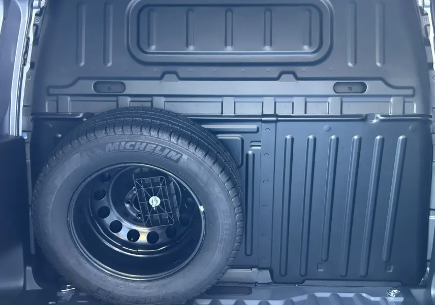 Vue intérieure du coffre du Dangel Peugeot Partner gris Artense, mettant en valeur la roue de secours fixée au panneau arrière.